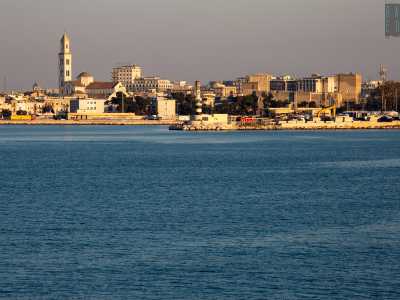 Sulla nostra sinistra appare lo skyline del centro storico di Bari, che sembra quasi galleggiare sul mare calmo e blu. In primo piano scorgiamo l�ottocentesco faro borbonico, mentre alle sue spalle si mostrano i massicci torrioni del Castello e la Cattedrale, con il suo alto campanile
